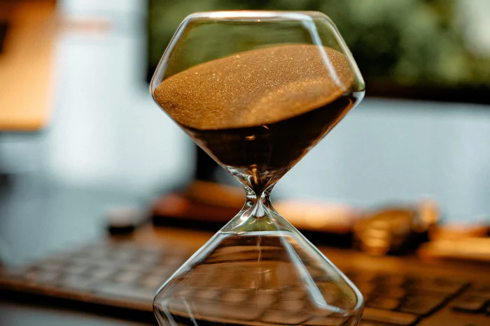 an hourglass with sand moving down, on a desk in front of a laptop