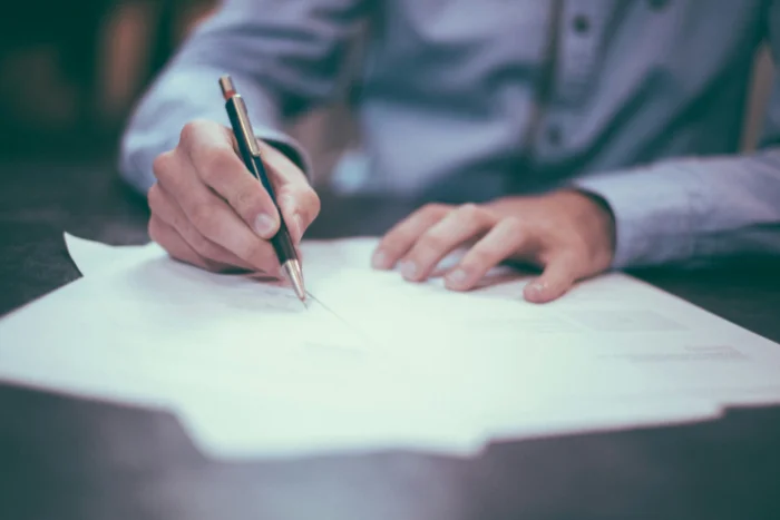 A man in a blue button up shirt writing while using a pen